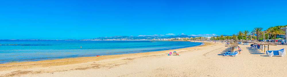 Immagine di una spiaggia soleggiata a Palma di Maiorca, Spagna, con sabbia bianca e acqua cristallina.